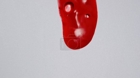 Photo for Liquid and gel creative advertisement concept. Close up shot of transparent substance on the white background. Red colored cosmetic product gel fluid or serum flowing on the clear surface. - Royalty Free Image