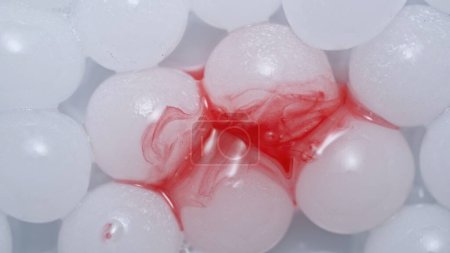 Téléchargez les photos : Beaucoup de sphères d'hydrogel blanc. Des sphères de gel rondes brillantes et un pigment rouge scintillent sur fond de studio blanc. Concept créatif de publicité cosmétique dans l'industrie de la beauté. - en image libre de droit