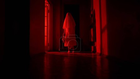 Photo for Horror movie and poltergeist creative advertisement concept. Portrait of ghost female in the house. Woman in white dress with veil covering her face walking holding a toy, red lightning. - Royalty Free Image