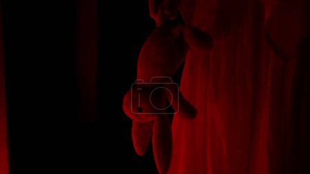 Foto de Película de terror y concepto de publicidad creativa poltergeist. Fantasma femenino en una casa. Una mujer con un vestido blanco está caminando por un pasillo sosteniendo un juguete. Luz roja de horror. De cerca. - Imagen libre de derechos