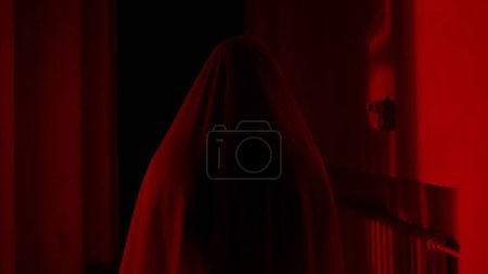 Photo for Horror movie and poltergeist creative advertisement concept. Portrait of ghost female in the house. Woman in white dress with veil covering her face walking in the corridor with red lightning - Royalty Free Image