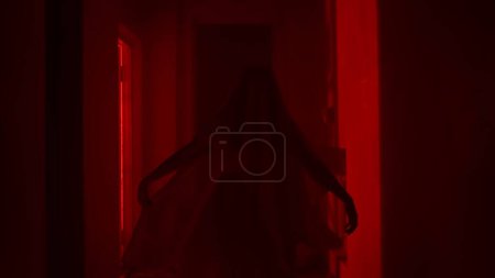 Photo for Horror movie and poltergeist creative advertisement concept. Portrait of ghost female in the house. Woman in white dress with veil covering her face walking in the corridor with red lightning - Royalty Free Image