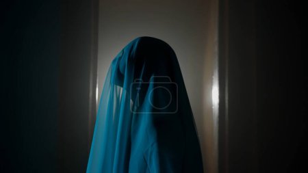 Photo for Horror movie and poltergeist creative advertisement concept. Portrait of ghost female in the house. Woman in white dress with veil covering her face walking in the room with blue lightning. - Royalty Free Image