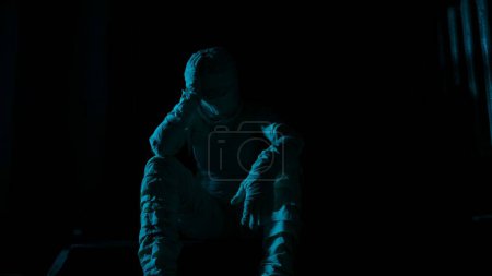 Photo for Horror movie and poltergeist creative advertisement concept. Portrait of ghost person in the house. Mummy covered in white cloth ribbons sitting on the staircase of the house looking at the camera. - Royalty Free Image