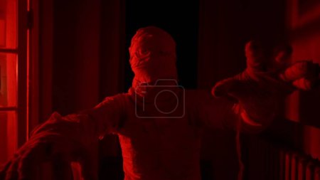 Photo for Horror movie and poltergeist creative advertisement concept. Portrait of ghost person in the house. Mummy covered in white cloth ribbons walking in the corridor with red flashing lightning. - Royalty Free Image