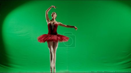 Téléchargez les photos : Ballet classique et moderne concept publicitaire créatif. Femme sur fond chromatique clé de l'écran vert. Belle ballerine en tutu rouge et pointes dansant sur les orteils chorégraphie en studio. - en image libre de droit