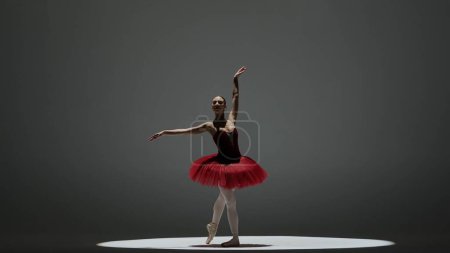 Foto de Concepto clásico y moderno de publicidad creativa de ballet. Retrato de mujer sobre fondo blanco en estudio bajo foco. Hermosa bailarina en tutú rojo bailando alrededor. - Imagen libre de derechos