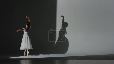 Klassisches und modernes Ballett kreatives Werbekonzept. Frauenporträt auf weißem Hintergrund im Studio im Scheinwerferlicht. Schöne Ballerina in weißem Tüll tanzt langsames Element der Choreographie.
