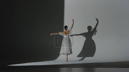 Klassisches und modernes Ballett kreatives Werbekonzept. Frauenporträt auf weißem Hintergrund im Studio im Scheinwerferlicht. Schöne Ballerina in weißem Tüll tanzt langsames Element der Choreographie.