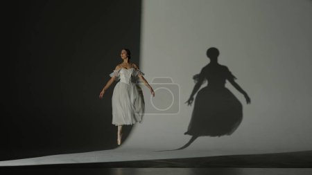 Foto de Concepto clásico y moderno de publicidad creativa de ballet. Retrato de mujer sobre fondo blanco en estudio bajo foco. Hermosa bailarina en tul blanco bailando elemento lento de la coreografía. - Imagen libre de derechos