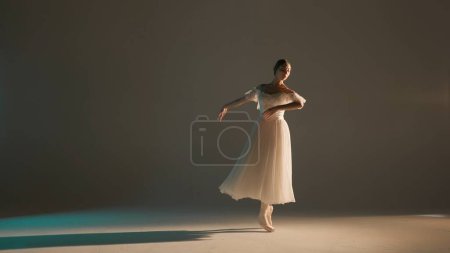 Foto de Concepto clásico y moderno de publicidad creativa de ballet. Retrato de mujer sobre fondo suave en luz cálida en estudio. Hermosa bailarina en tul blanco que muestra el elemento de danza de la coreografía. - Imagen libre de derechos