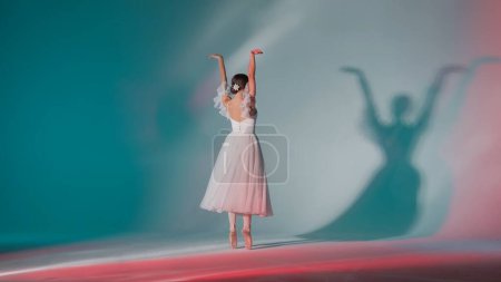 Photo for Classical and modern ballet creative advertisement concept. Portrait of female on green background in pink neon light studio. Young ballerina in white tulle showing beautiful element of choreography. - Royalty Free Image
