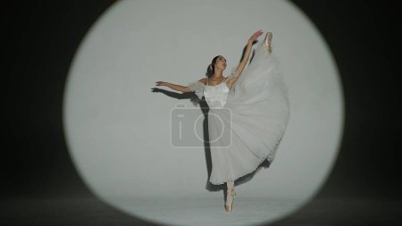 Klassisches und modernes Ballett kreatives Werbekonzept. Frauenporträt auf weißem Hintergrund im Studio im hellen Scheinwerferlicht. Elegante Ballerina in weißem Tülltanz mit hohem Split-Element.