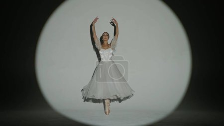 Photo for Classical and modern ballet creative advertisement concept. Portrait of female on white background in studio in bright spotlight. Elegant ballerina in white tulle dancing showing high split element. - Royalty Free Image
