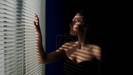 Photo for Beauty of body creative advertisement concept. Portrait of beautiful female model in the studio. Attractive woman silhouette standing near window with reflection from jalousie touching it with hand. - Royalty Free Image