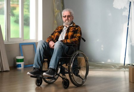 Photo for The shot shows a room in which a renovation is taking place, it is unfinished. In the center of the room sits a man in a wheelchair. Concept of life of a person with disability - Royalty Free Image