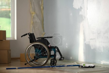 Photo for In the picture there is an empty room in which repair is taking place, it is incomplete. There is an empty wheelchair by the wall. Next to it there is an understated wall in white paint. General plan. - Royalty Free Image