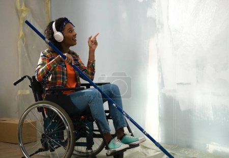 Foto de La imagen muestra la habitación en la que se realiza la reparación. Una mujer adulta en silla de ruedas. Ella está en la reparación de auriculares, pintando paredes con un rodillo - Imagen libre de derechos