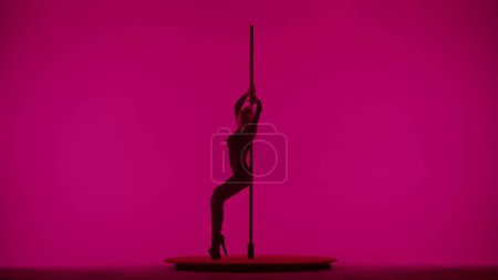 Photo for Modern dance style and choreography creative concept. Portrait of young female dancer in the studio. Professional pole dancer girl dancing on pylon, showing modern pole dance, pink neon background. - Royalty Free Image