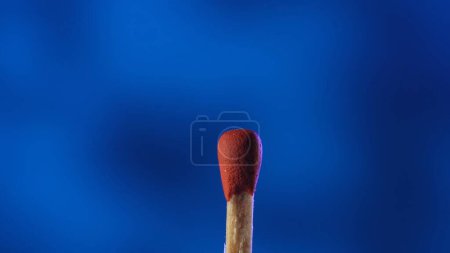 Photo for A macro shot of a matchstick against a blue background. A wooden match with red sulfur - Royalty Free Image