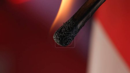Foto de Macro disparo de un partido en llamas contra un fondo de estudio rojo. La llama de la cerilla encendida ilumina el espacio oscuro. El fósforo ardiente está envuelto en una llama naranja - Imagen libre de derechos