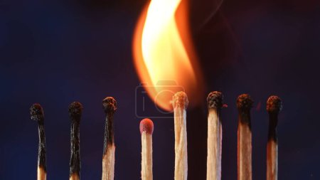 Foto de Una fila de fósforos donde dos fósforos en llamas pasan su fuego al siguiente. Cascada de llama, transferencia de energía. Macro disparo de la transición de la llama de un partido a otro - Imagen libre de derechos
