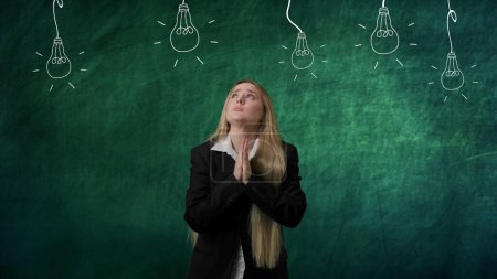 Photo for Imagination in problem solving concept. Portrait of woman isolated on green background light bulbs image on top. Girl standing thinking looking up with praying gesture, no ideas lamps without light. - Royalty Free Image