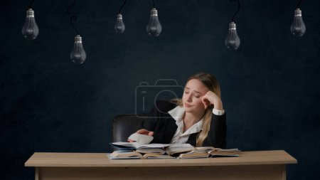 Foto de Retrato de niña sobre bombillas de fondo aisladas colgando en la parte superior. Chica triste sentada en una mesa con muchos libros. Molesto porque no hay ideas, las bombillas no brillan - Imagen libre de derechos