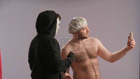 Téléchargez les photos : Un homme avec un torse nu portant un bonnet de douche prend des selfies avec un maniaque. Un maniaque armé d'un couteau a attaqué un baigneur sous la douche - en image libre de droit