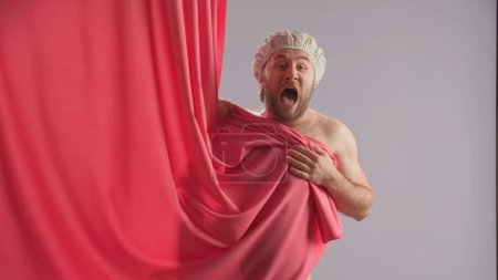 Téléchargez les photos : Homme effrayé à moitié déshabillé en casquette imperméable criant et se cachant derrière un rideau de douche rose, gros plan. Concept d'hygiène - en image libre de droit