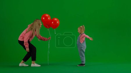 Photo for Children creative concept. Portrait of small girl in studio. Little girl standing with closed eyes, mom brings her balloons, girl is happy and surprised on chroma key green screen background. - Royalty Free Image