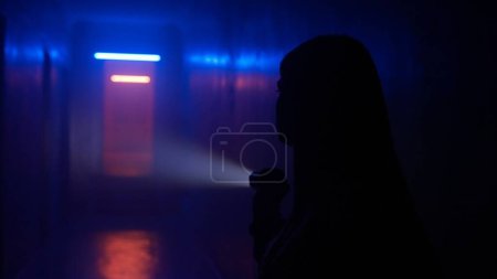 Photo for Abandoned places and empty buildings creative advertisement concept. Portrait of female in the dark hallway with neon light. Woman with flashlight standing in the corridor and exploring, looks around. - Royalty Free Image