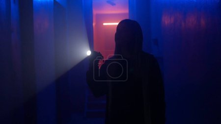 Téléchargez les photos : Lieux abandonnés et bâtiments vides concept publicitaire créatif. Portrait de femme dans le couloir sombre avec lumière au néon. Femme avec lampe de poche debout dans le couloir et explorer, regarde autour de. - en image libre de droit