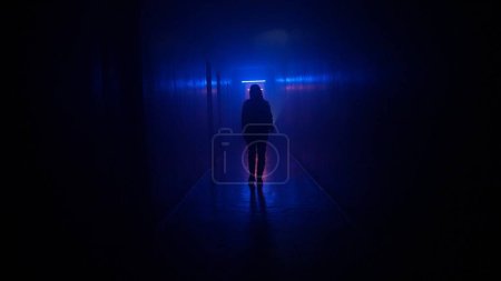 Photo for Abandoned places and empty buildings creative advertisement concept. Portrait of female in the dark hallway with neon light. Woman with flashlight walking down the corridor with door and staircase. - Royalty Free Image