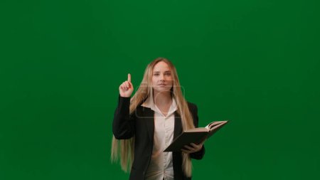 Photo for Brainstorming and problem solving concept. Portrait of female on chroma key green screen. Girl standing reading notebook, finding idea raising finger up, lamp lights up over head, positive expression. - Royalty Free Image