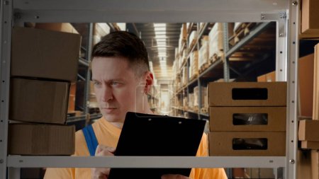 Photo for Business warehouse and logistics advertisement concept. Portrait of male model working in storage. Man storekeeper standing near rack with boxes, watching social media on tablet. - Royalty Free Image