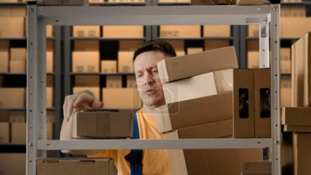 Photo for Business warehouse and logistics creative advertisement concept. Portrait of male working in storage. Man storekeeper standing near rack taking boxes holding big stack in hands and dropping packages. - Royalty Free Image