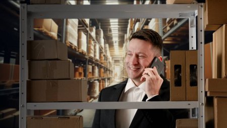 Photo for Business warehouse and logistics creative advertisement concept. Portrait of storekeeper working in storage. Man manager in formal outfit near rack goods talking on smartphone, positive expression. - Royalty Free Image