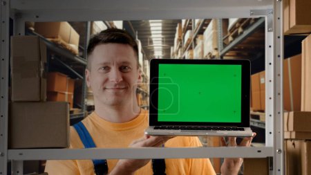 Photo for Business warehouse and logistics creative advertisement concept. Portrait of male working in storage. Man storekeeper standing near rack with boxes holding laptop with chroma key green screen mockup. - Royalty Free Image