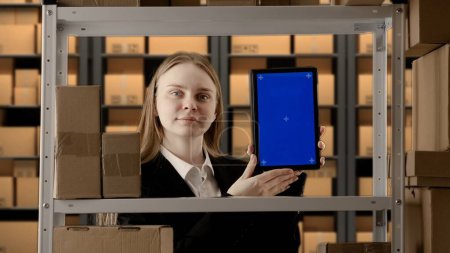 Photo for Business warehouse and logistics creative concept. Portrait of female working in storage. Storekeeper manager in formal outfit near rack with boxes holding tablet with blue screen workspace mockup. - Royalty Free Image