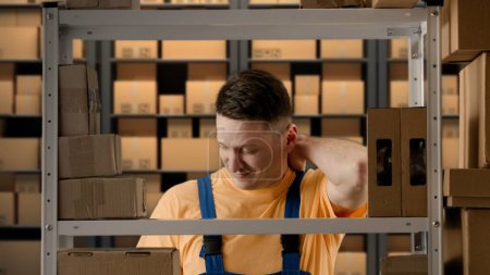 Photo for Business warehouse and logistics creative advertisement concept. Portrait of male working in storage. Man storekeeper standing near rack with boxes tired face massaging neck has back pain after work. - Royalty Free Image