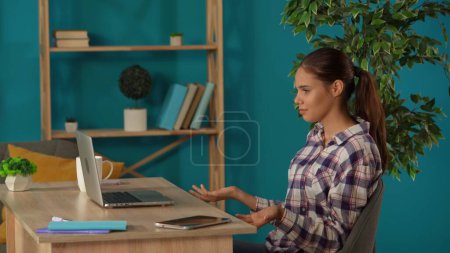 Photo for Medium shot capturing a woman having a videocall, talking to somebody on a laptop in her home office. Young female programmer, businesswoman working. Remote job, modern lifestyle. - Royalty Free Image
