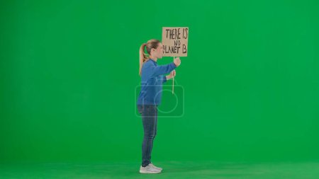 Téléchargez les photos : Vue latérale d'une militante hurlante tenant une pancarte disant "Il n'y a pas de planète B". Une manifestante avec une pancarte sur un écran vert. Sauver la planète, le réchauffement climatique et le changement climatique - en image libre de droit