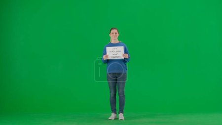Photo for A young woman activist holds a poster that says Lets build a better world together. Portrait of female protester holding donation box on green screen - Royalty Free Image