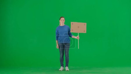Photo for A sad female activist holds a blank sign on a green screen. Chroma key, advertisement, promo - Royalty Free Image