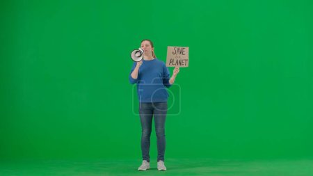 Photo for A woman speaks into a megaphone and holds a placard that reads Save Our Planet. Woman with a mouthpiece and a poster on a green screen. Save planet, climate changes concept, ecology. Advertising - Royalty Free Image