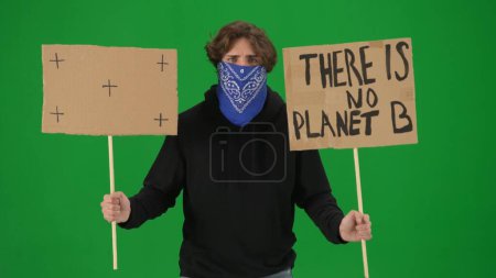 Téléchargez les photos : Un manifestant masculin avec son visage couvert d'une écharpe tient un panneau indiquant qu'il n'y a pas de planète B et un panneau vierge. L'homme activiste sur un écran vert de près. Clé chromatique - en image libre de droit