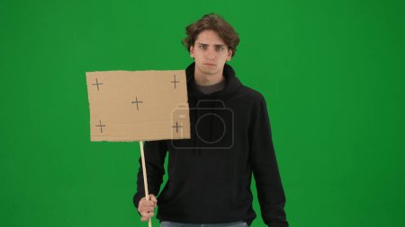 Téléchargez les photos : Un militant masculin triste tient de près une affiche vierge sur un écran vert. Clé chromatique, publicité, promo - en image libre de droit