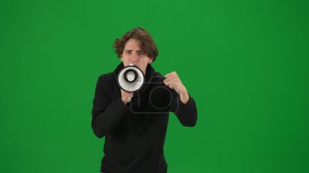 Photo for Male activist with raised fist shouting menacingly into megaphone in studio on green screen. Front view of a pro protest man close up. Protest action, fight for human rights, strike. Advertising - Royalty Free Image