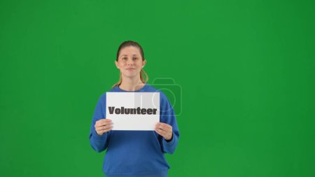Téléchargez les photos : Une femme tenant une affiche avec le mot Volontaire en gros plan. Portrait d'une bénévole sur un écran vert en gros plan. Aider les gens - en image libre de droit